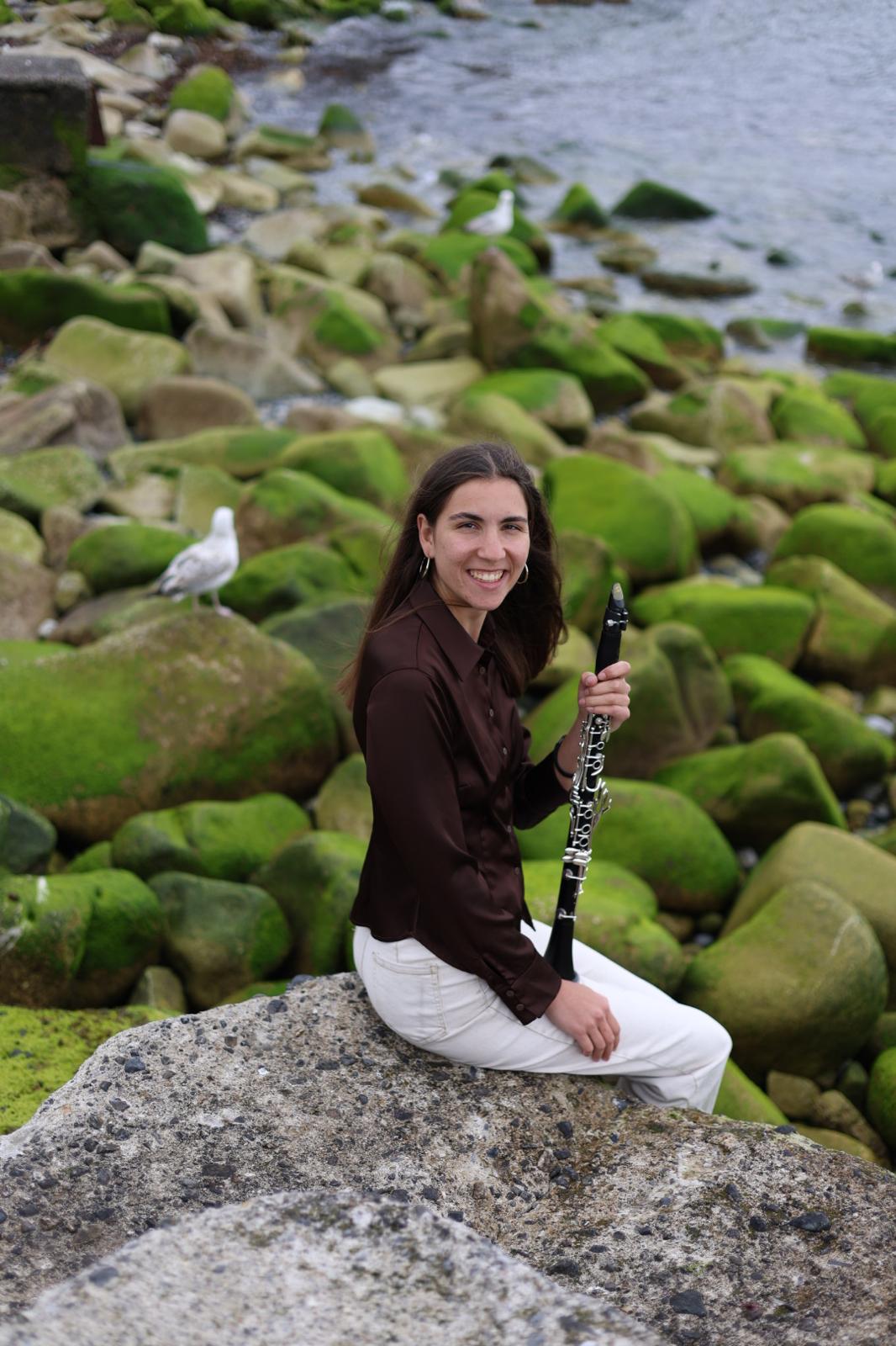 Margot Maurel seated by the coast holding her clarinet